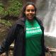 Karina Beras Standing in front of a waterfall with a green Hotelies are Gorges shirt